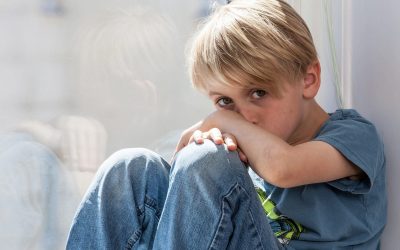 En lyshåret dreng sidder i en vindueskarm og kigger ind i kameraet