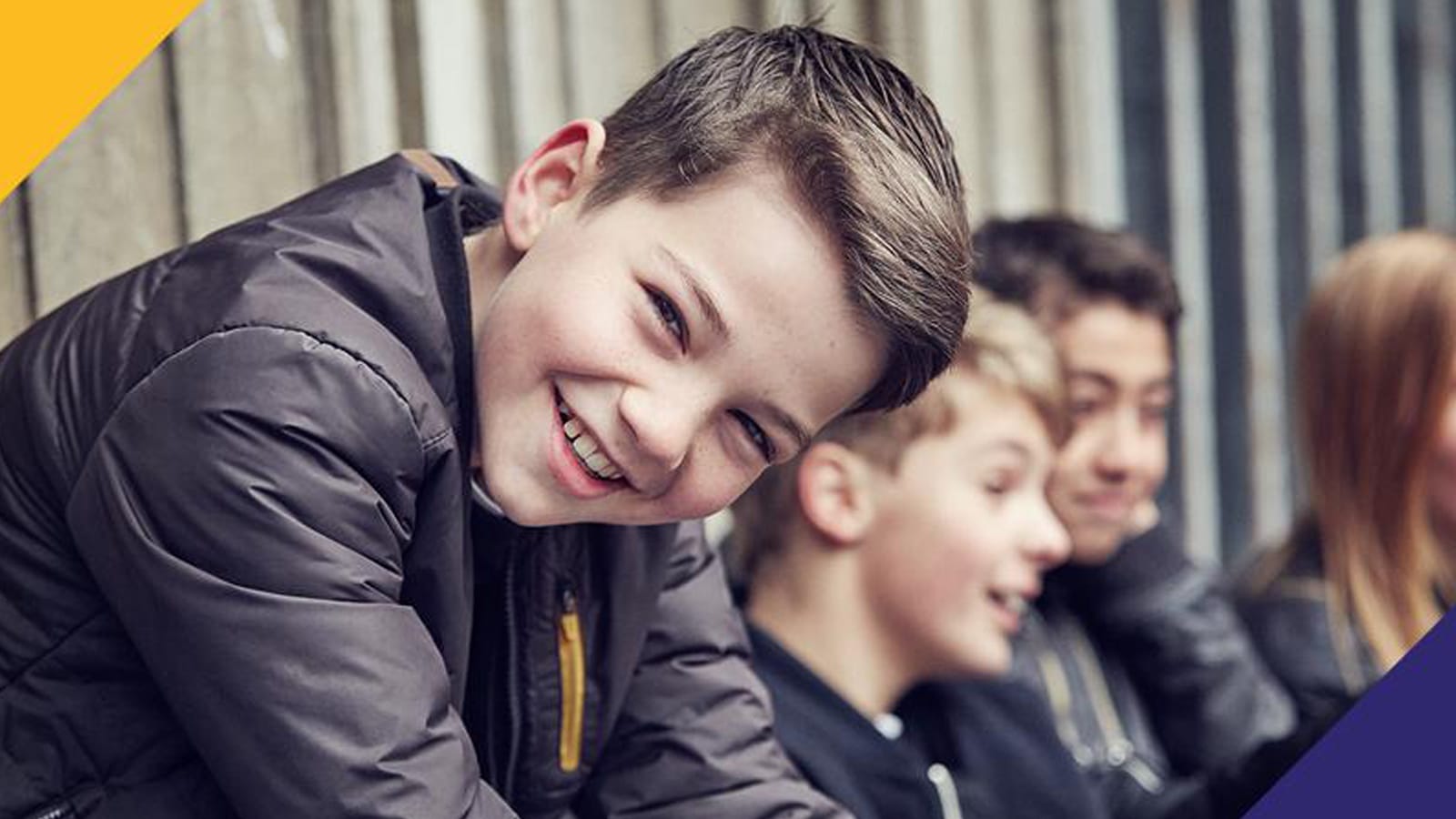 En mørkhåret dreng kigger smilende ind i kameraet, med tre børn i baggrunden.