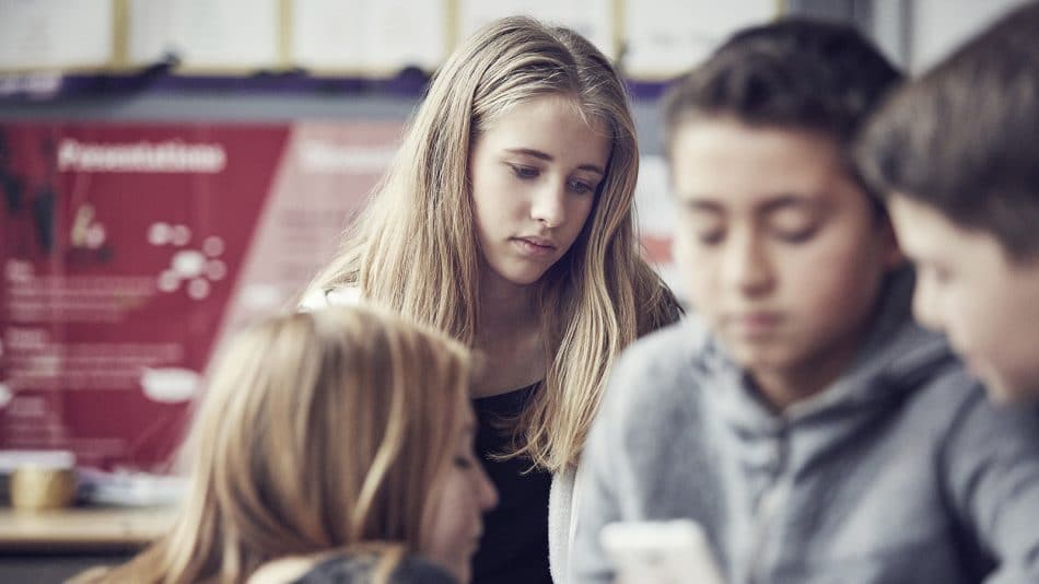 Lyshåret pige kigger til siden, mens slørede børn taler i forgrunden.