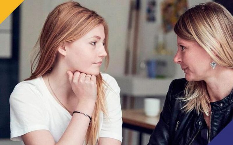 En rådhåret pige og en lyshåret dame kigger hinanden i øjnene.