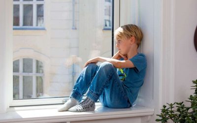 En lyshåret dreng sidder i en vindueskarm og kigger ud på gaden