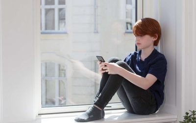 Dreng alene i vindueskarm med telefon.