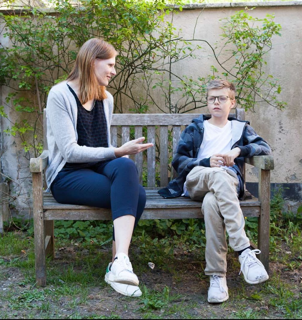 Brunhåret dame taler med lyshåret dreng på en bænk.
