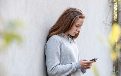 Brunhåret pige står op ad en væg og kigger ned i sin telefon