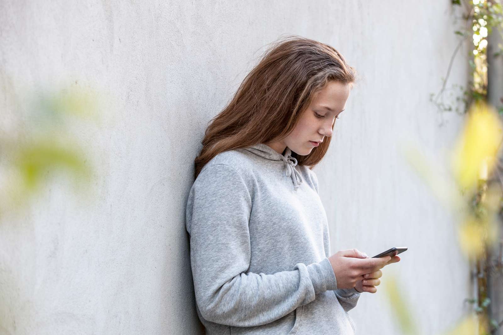 Brunhåret pige står op ad en væg og kigger ned i sin telefon