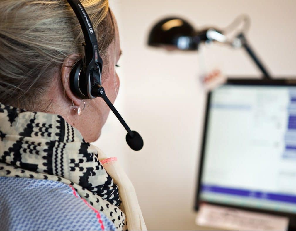 Lyshåret kvinde med headset på kigger på en skærm.