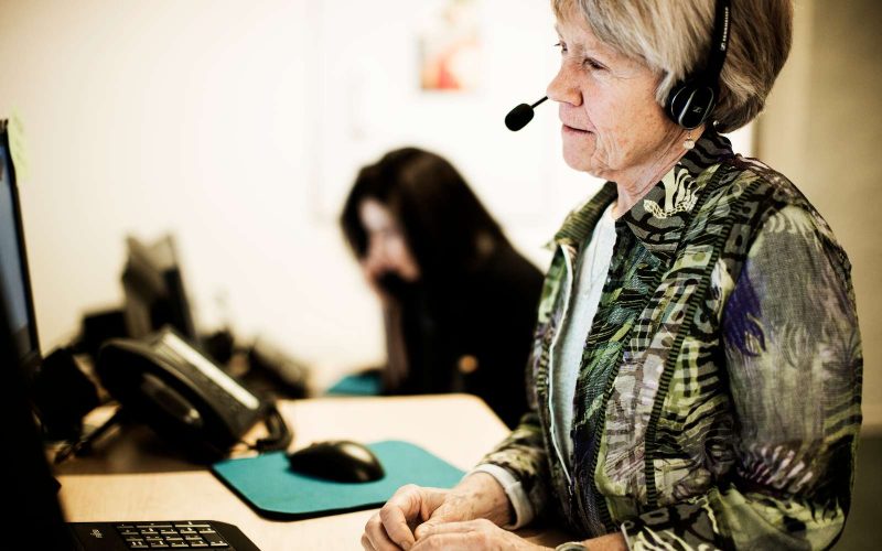 Ældre kvinde med høretelefoner på sidder foran en skærm