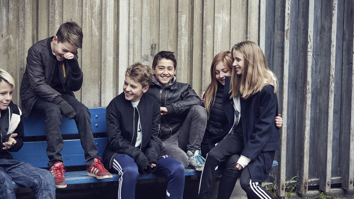 Seks børn sidder på en bænk og griner.