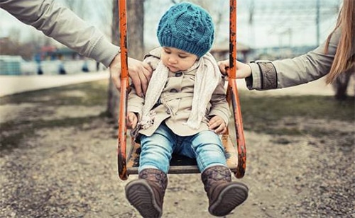 Barn på gynge bliver holdt af en hånd hver fra far og mor