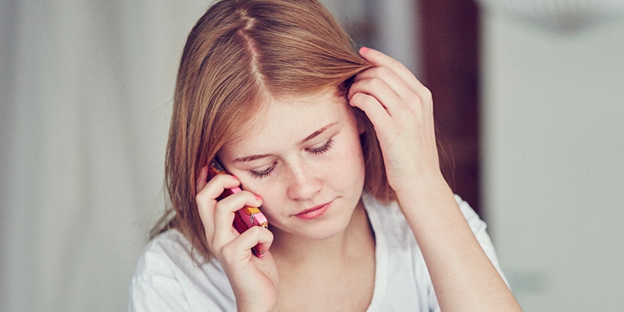 Rødhåret pige kigger ned, mens hun taler i telefon