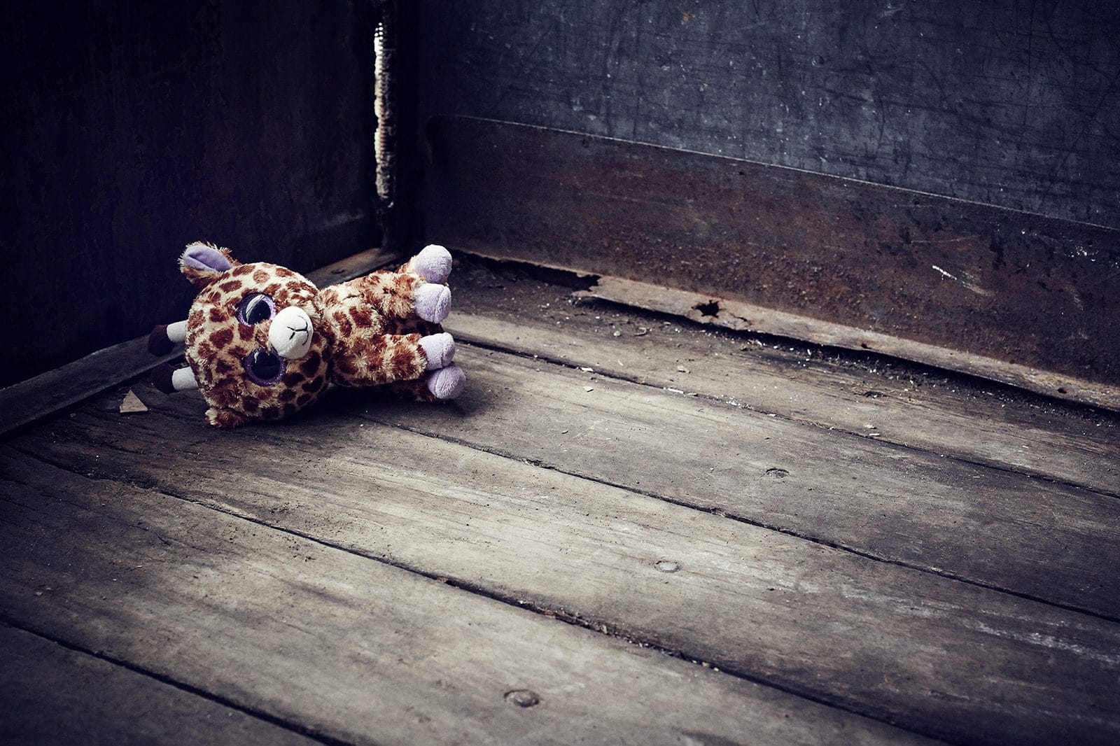En girafbamse ligger i et hjørne på et trægulv