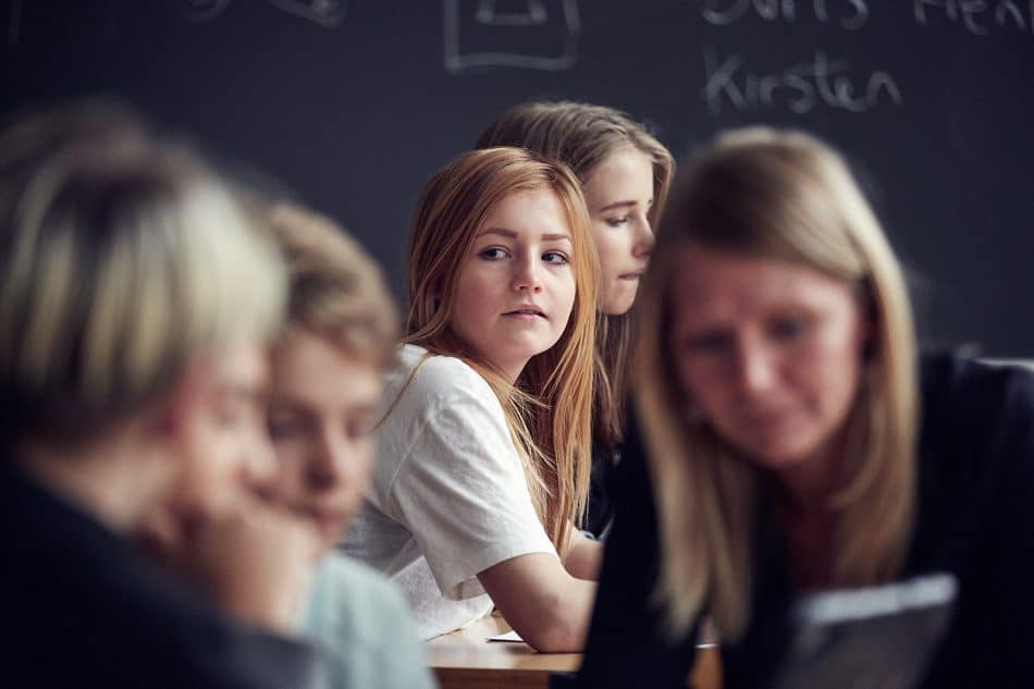 Rødhåret pige sidder alene i klasselokale i kigger ud til siden