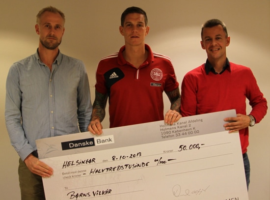 Tre mænd står foran en hvid væg med en cheque