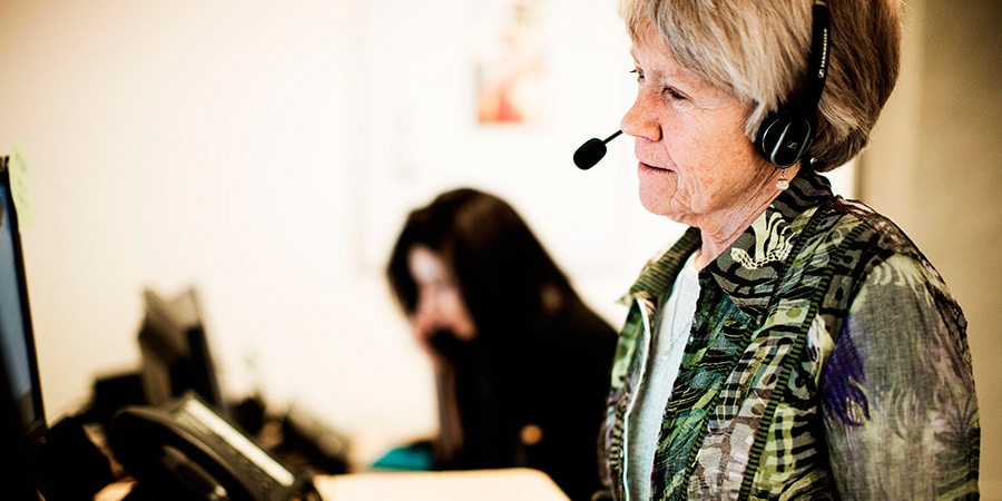 Ældre kvinde med headset på sidder foran en skærm