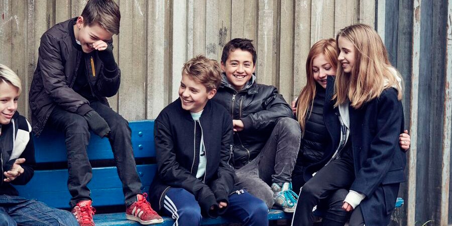 En gruppe unge sidder og griner på en bænk