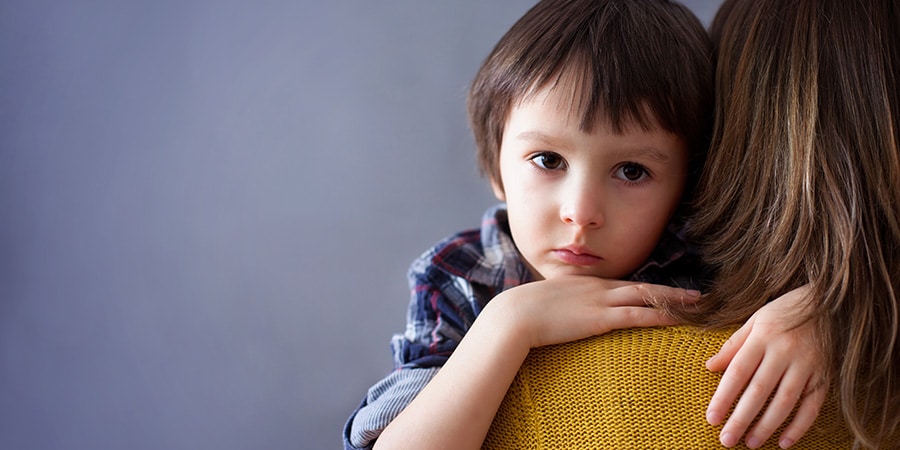 Brunhåret dreng kigger i kameraet, mens han krammer kvinde i gul sweater