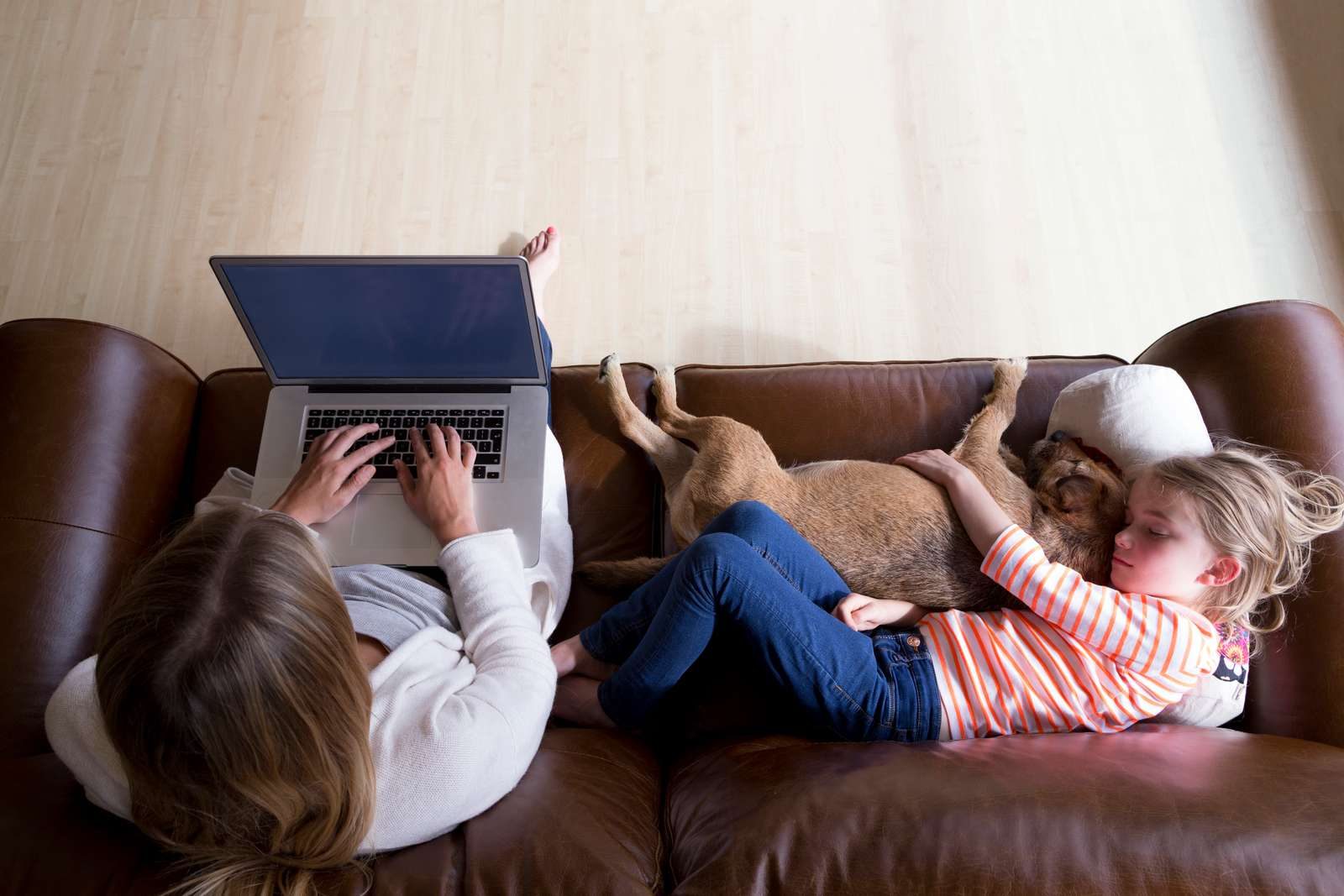 En kvinde sidder på en sofa med sin computer mens et barn sover ved siden af