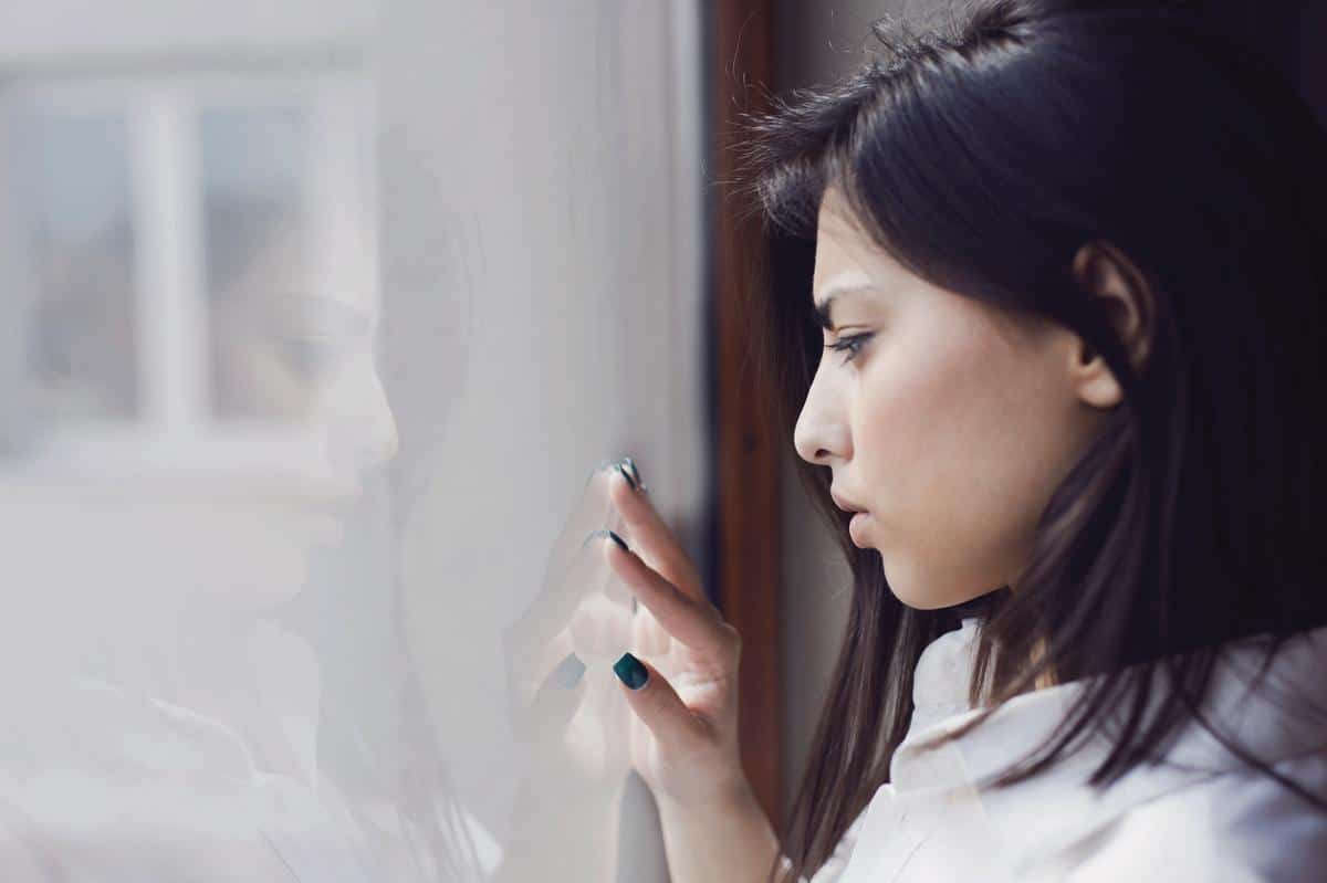 Pige med mørkt hår kigger ud ad vinduet og har hånden på ruden