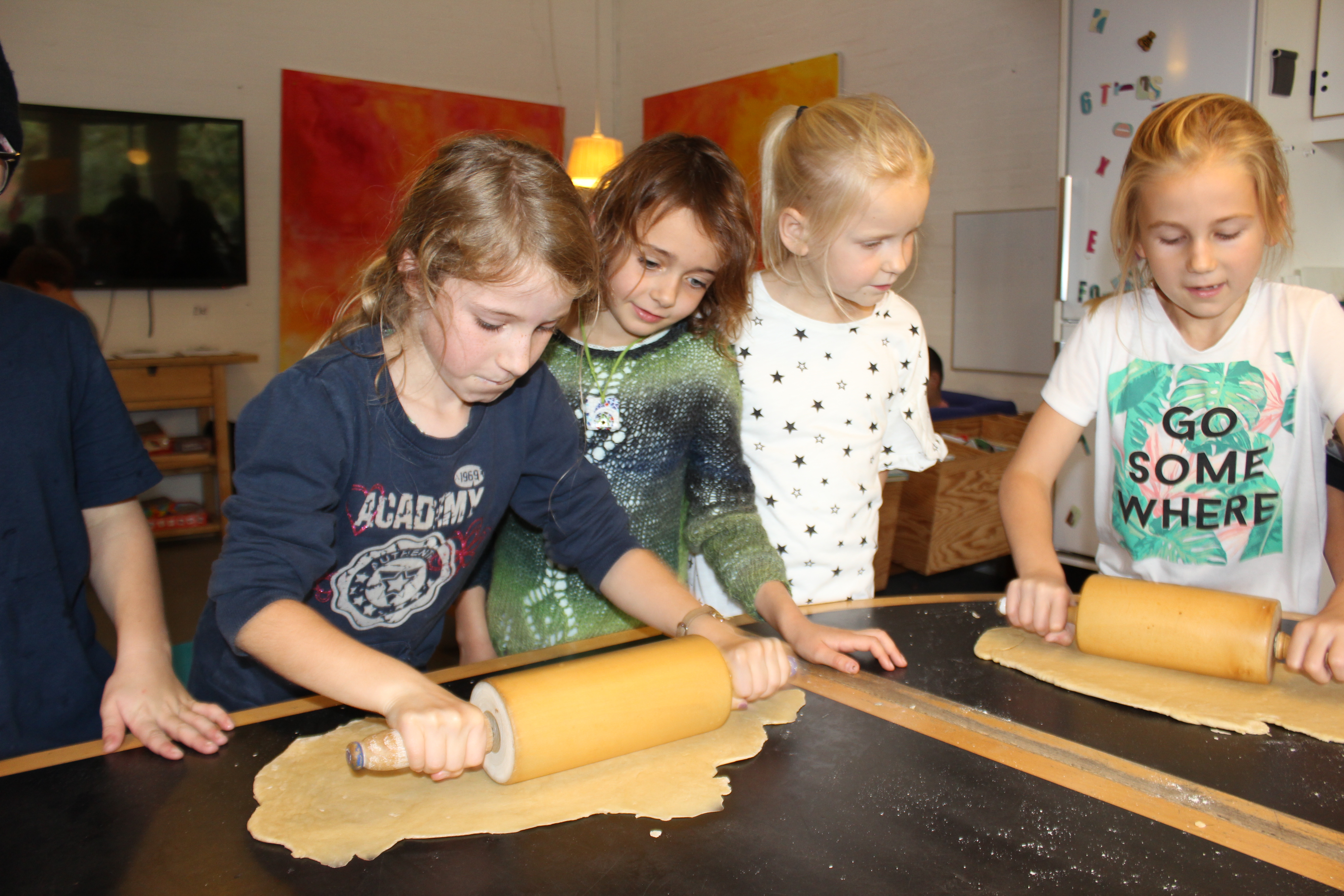 Fem børn ruller dej ud på et bord