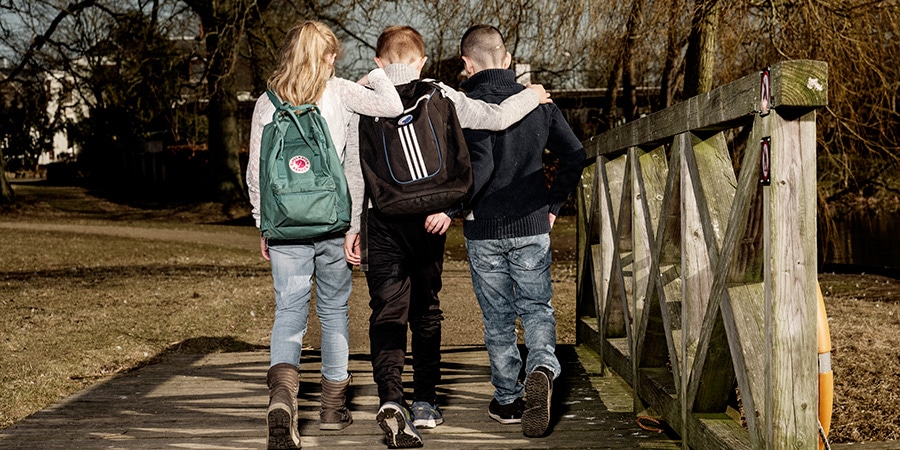 Tre børn set bagfra går over en bro