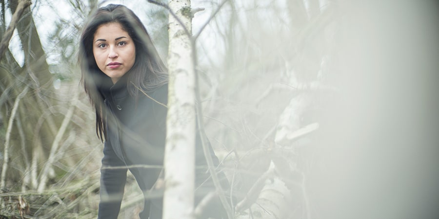 Mørkhåret kvinde ude i en skov kigger ind i kameraet