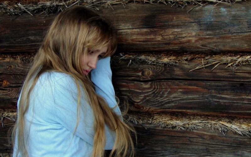 Trist pige læner sig op af trævæg