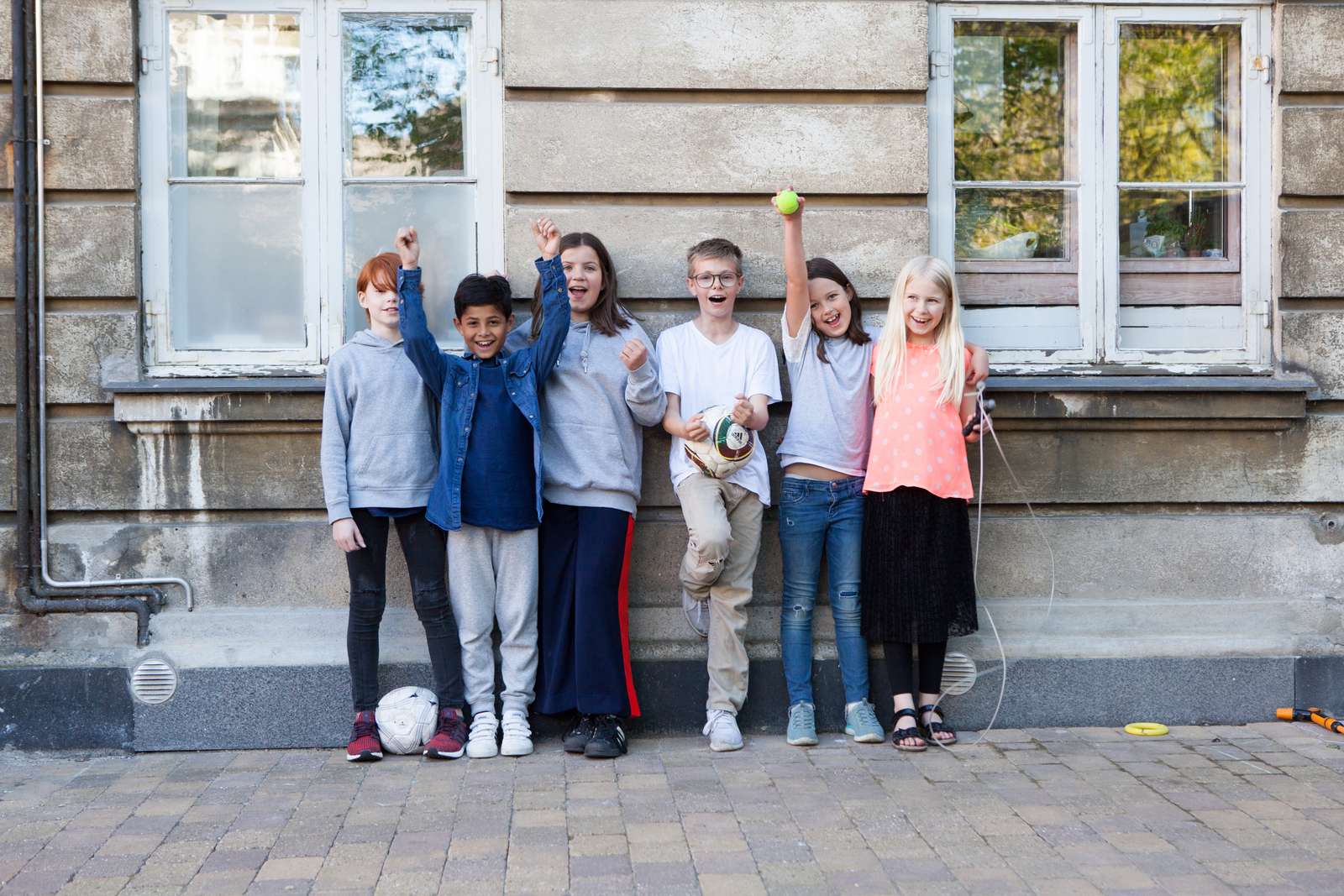 Seks børn der jubler foran en væg på en bygning.