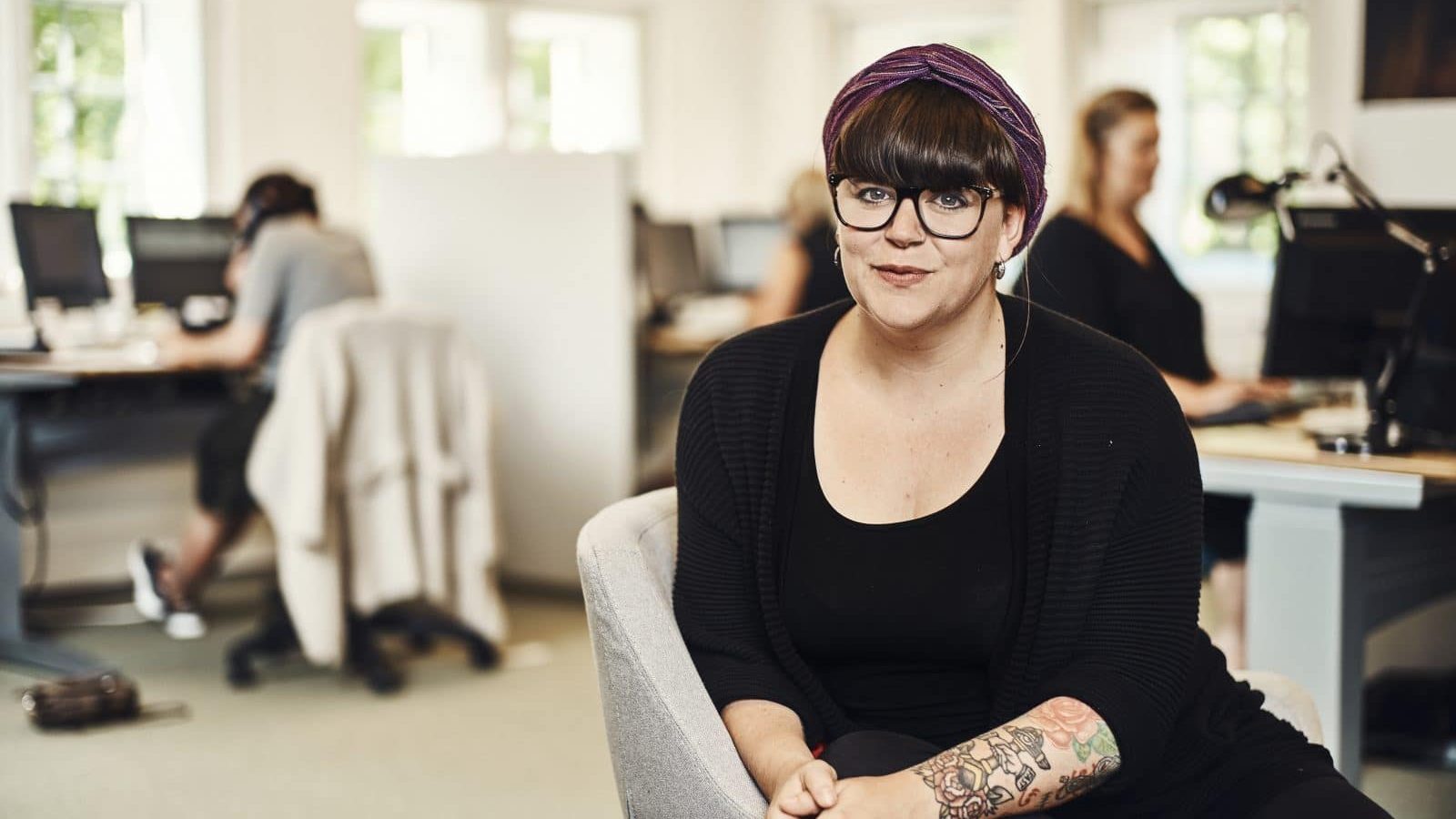 Mørkhåret kvinde med briller sidder på en stol og kigger ind i kameraet