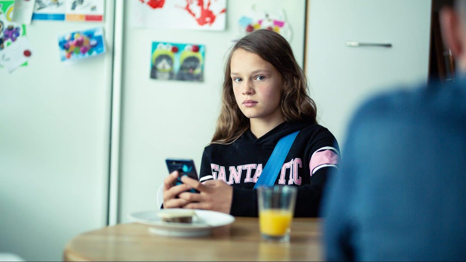 Pige kigger direkte ind i kameraet mens hun sidder med sin mobiltelefon i hånden