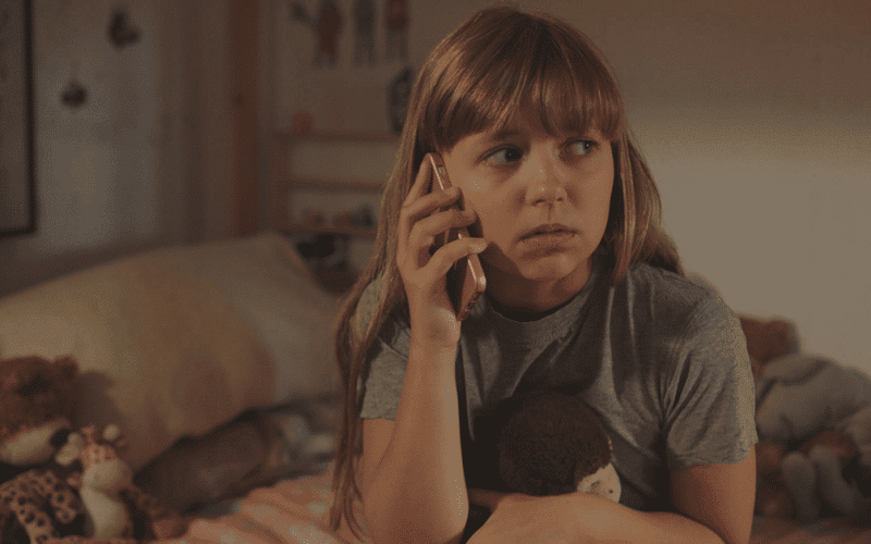 Blond pige sidder på sin seng og taler i telefon