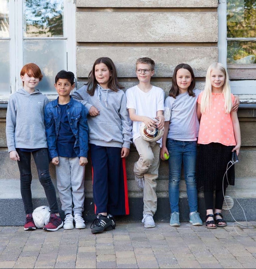 Seks børn står foran en mur