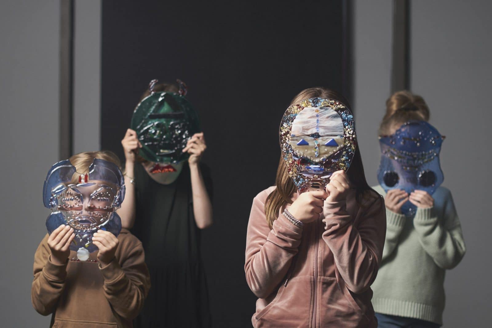 Fire børn står med masker holdt foran ansigtet