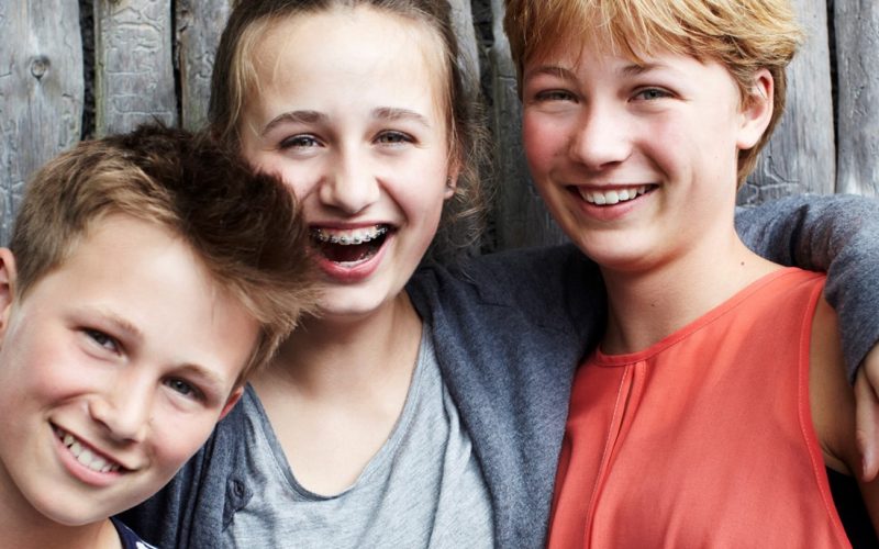 Tre unge står foran et hegn og smiler til kameraet