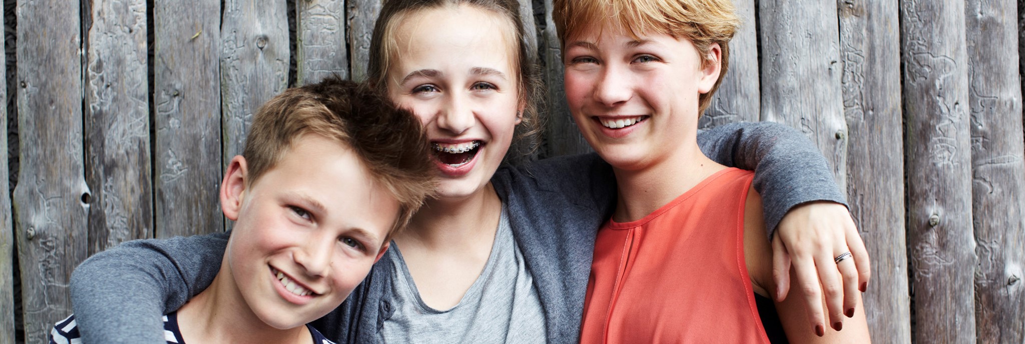 Tre unge står foran et hegn og smiler til kameraet