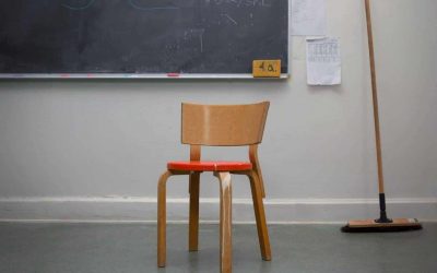 En stol af tre med rødt sæde står i hjørnet af et klasselokale, med en kost og en tavle i baggrunden.