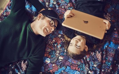 Far og datter ligger på en lilla dyne, hvor datteren holder en iPad