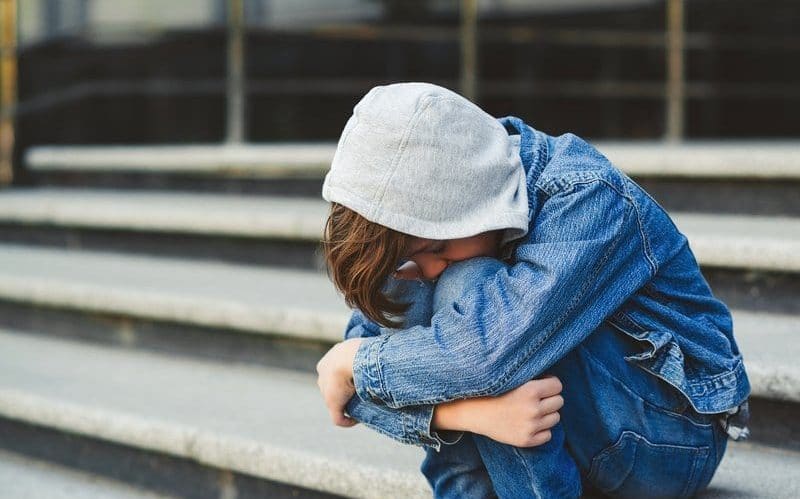 Dreng med hætte i sidder på hug på en trappe