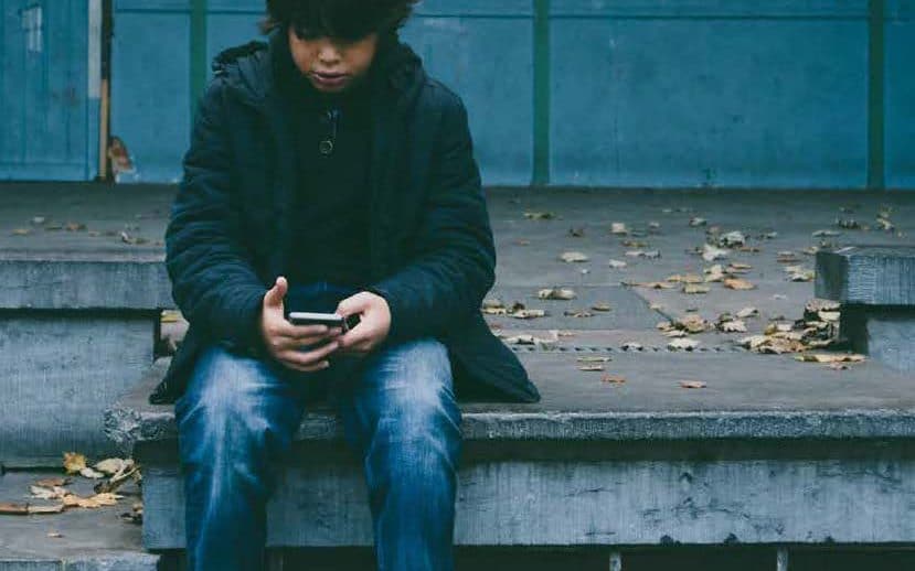 Mørkhåret dreng sidder udenfor og kigger ned i sin telefon