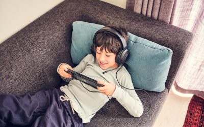 Mørkhåret dreng med headset på ligger på en sofa og kigger på Nintendo Switch