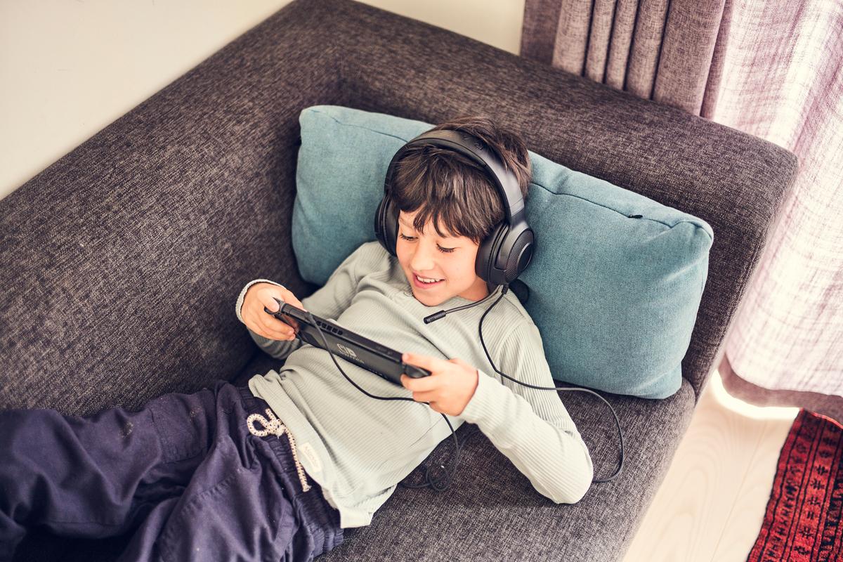 Mørkhåret dreng med headset på ligger på en sofa og kigger på Nintendo Switch