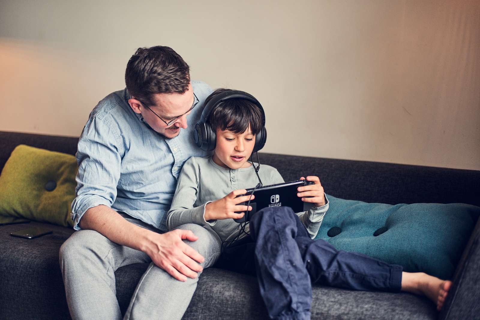 Mand og dreng sidder på en sofa og kigger på en Nintendo Switch