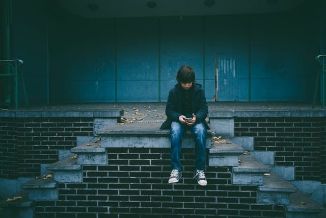 Dreng sidder udenfor på toppen af en trappe og kigger ned i sin telefon