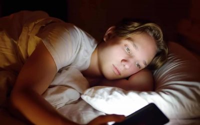 Dreng ligger i sin seng og kigger på sin telefon
