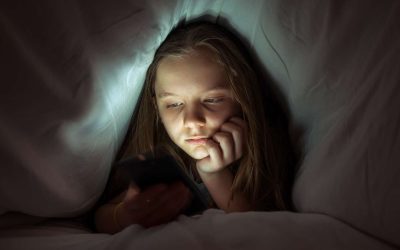 Pige dækket af dyne kigger på sin telefon