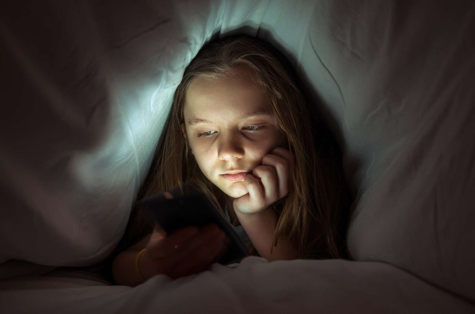 Pige dækket af dyne kigger på sin telefon