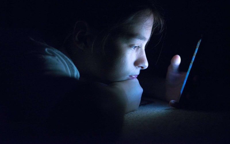 Pige ligger i mørke og kigger på sin telefon