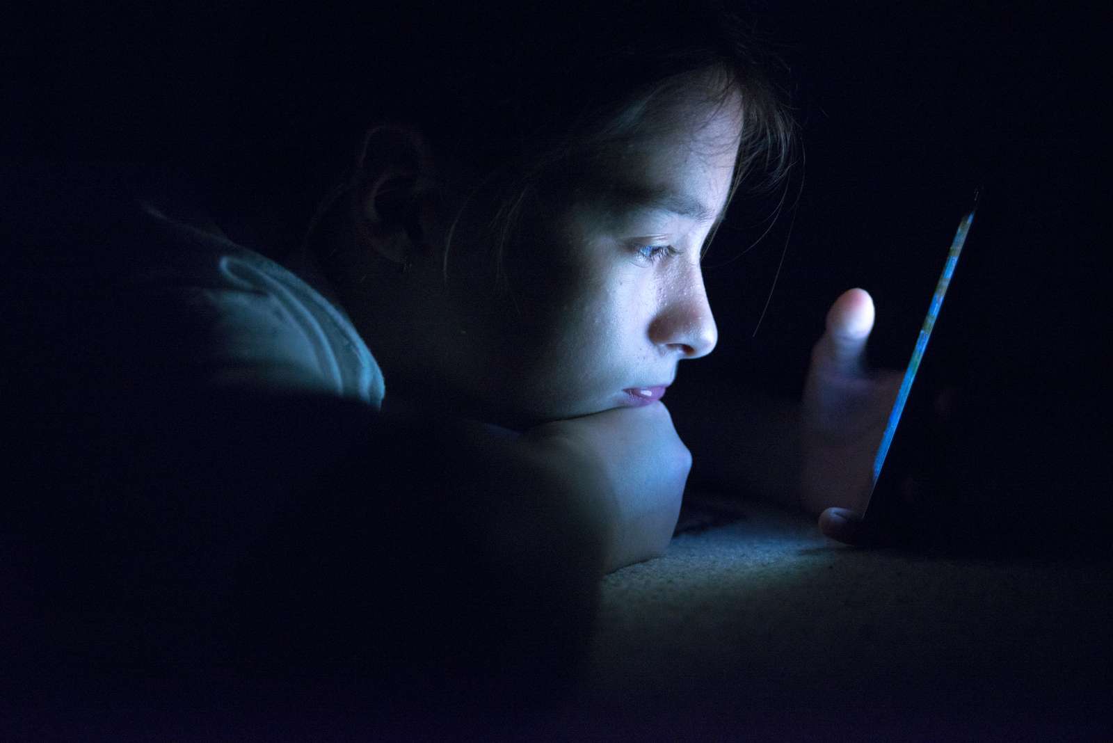 Pige ligger i mørke og kigger på sin telefon