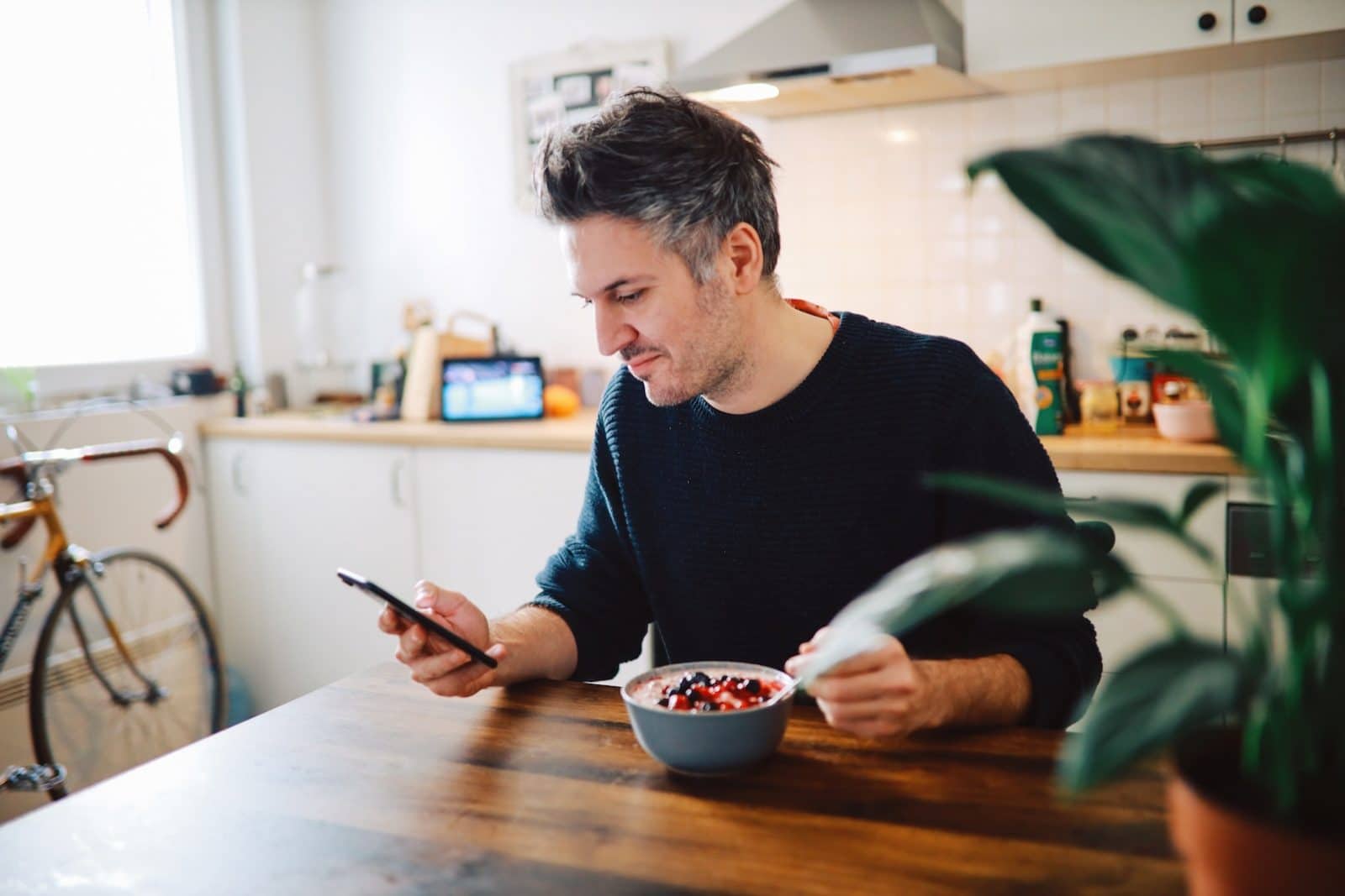 Mørkhåret mand sidder foran en fyldt skål og kigger på sin telefon.