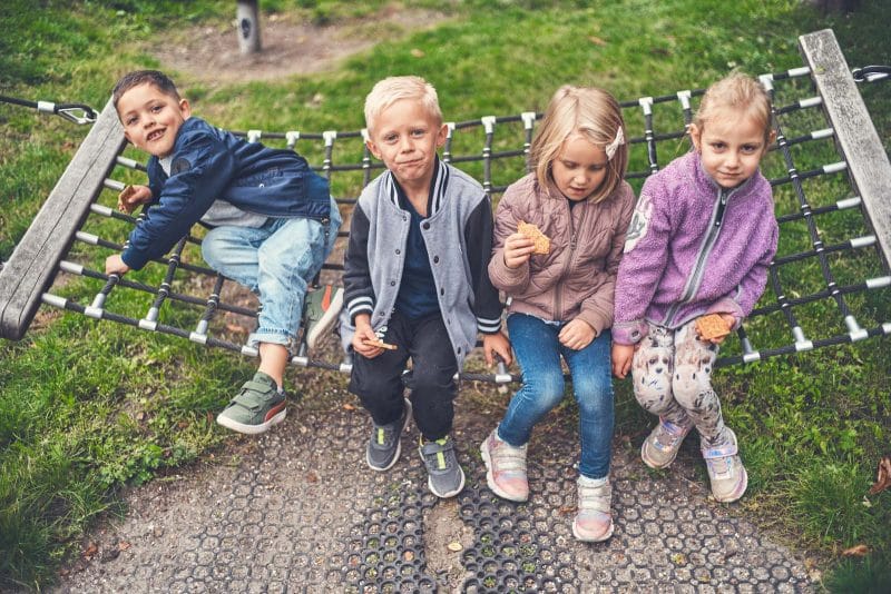 Fire børn sidder på en gynge og spiser kiks