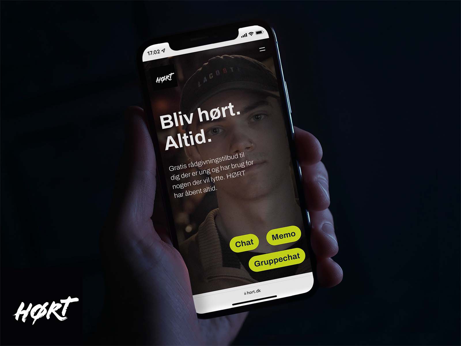 Hånd holder en mobil med HØRTs hjemmeside på